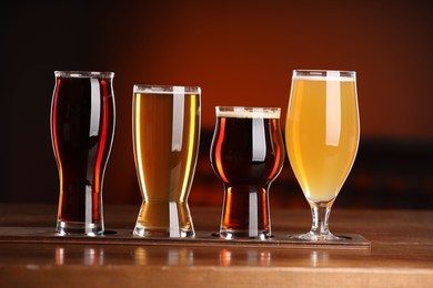 Photo of Glasses with different types of beer on wooden table against color background