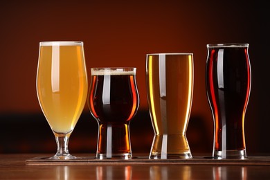 Photo of Glasses with different types of beer on wooden table against color background