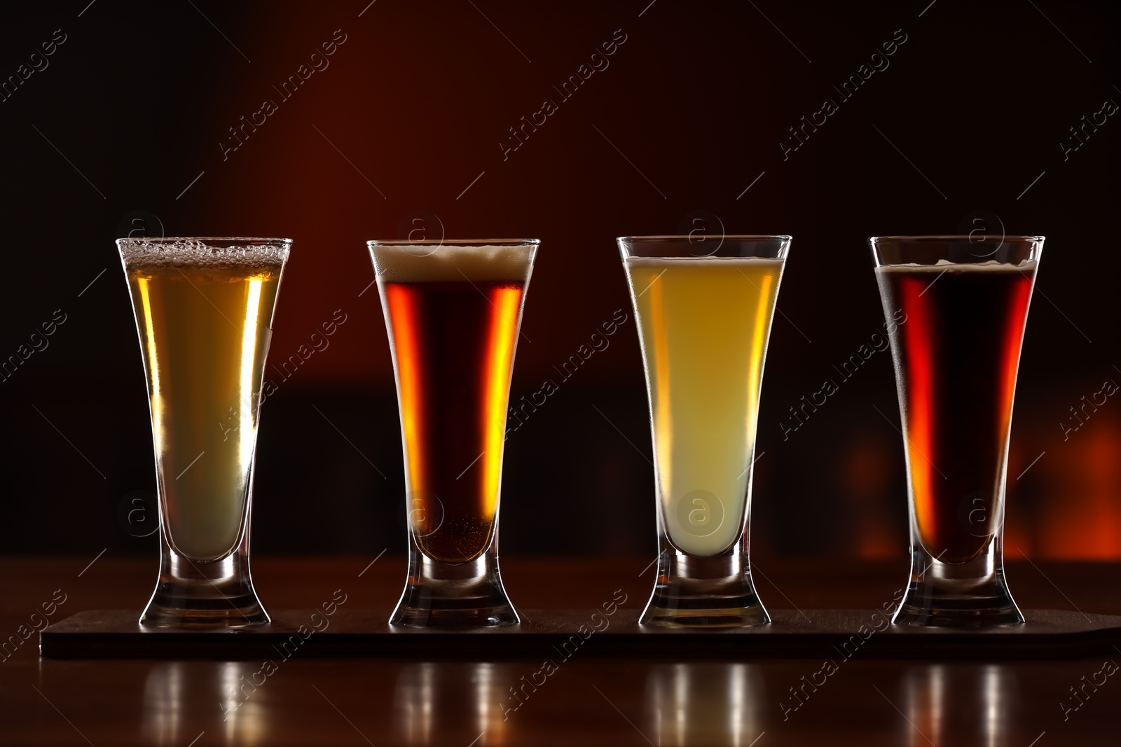 Photo of Glasses with different types of beer on wooden table against color background