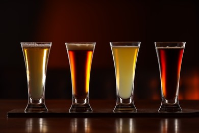 Glasses with different types of beer on wooden table against color background