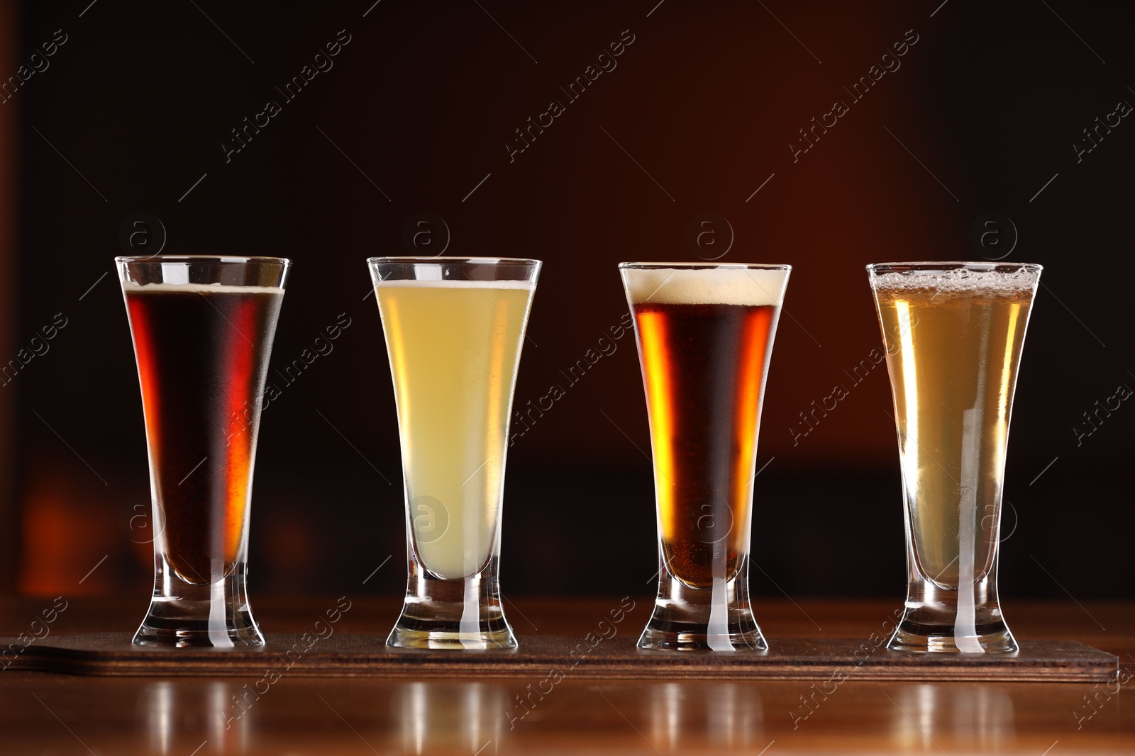 Photo of Glasses with different types of beer on wooden table against color background