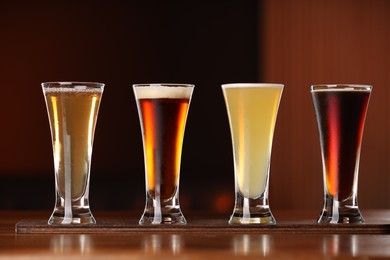 Photo of Glasses with different types of beer on wooden table against color background