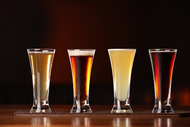 Photo of Glasses with different types of beer on wooden table against color background