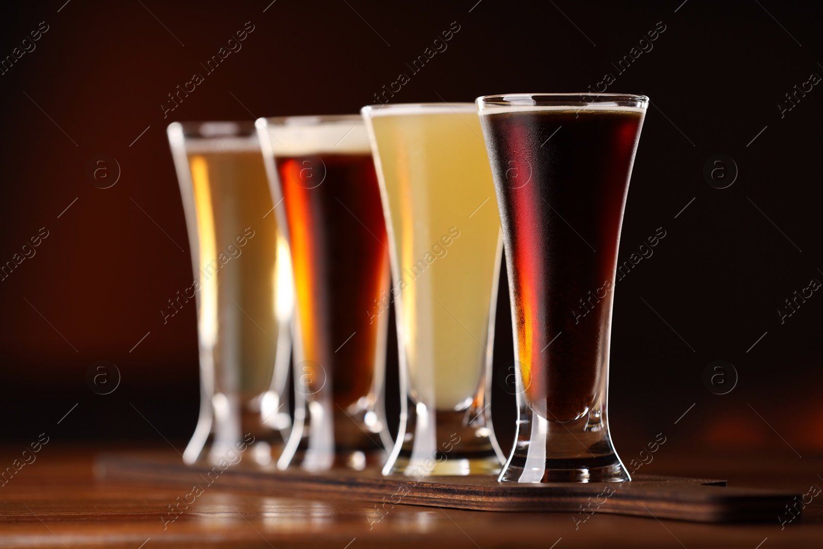 Photo of Glasses with different types of beer on wooden table against color background, closeup