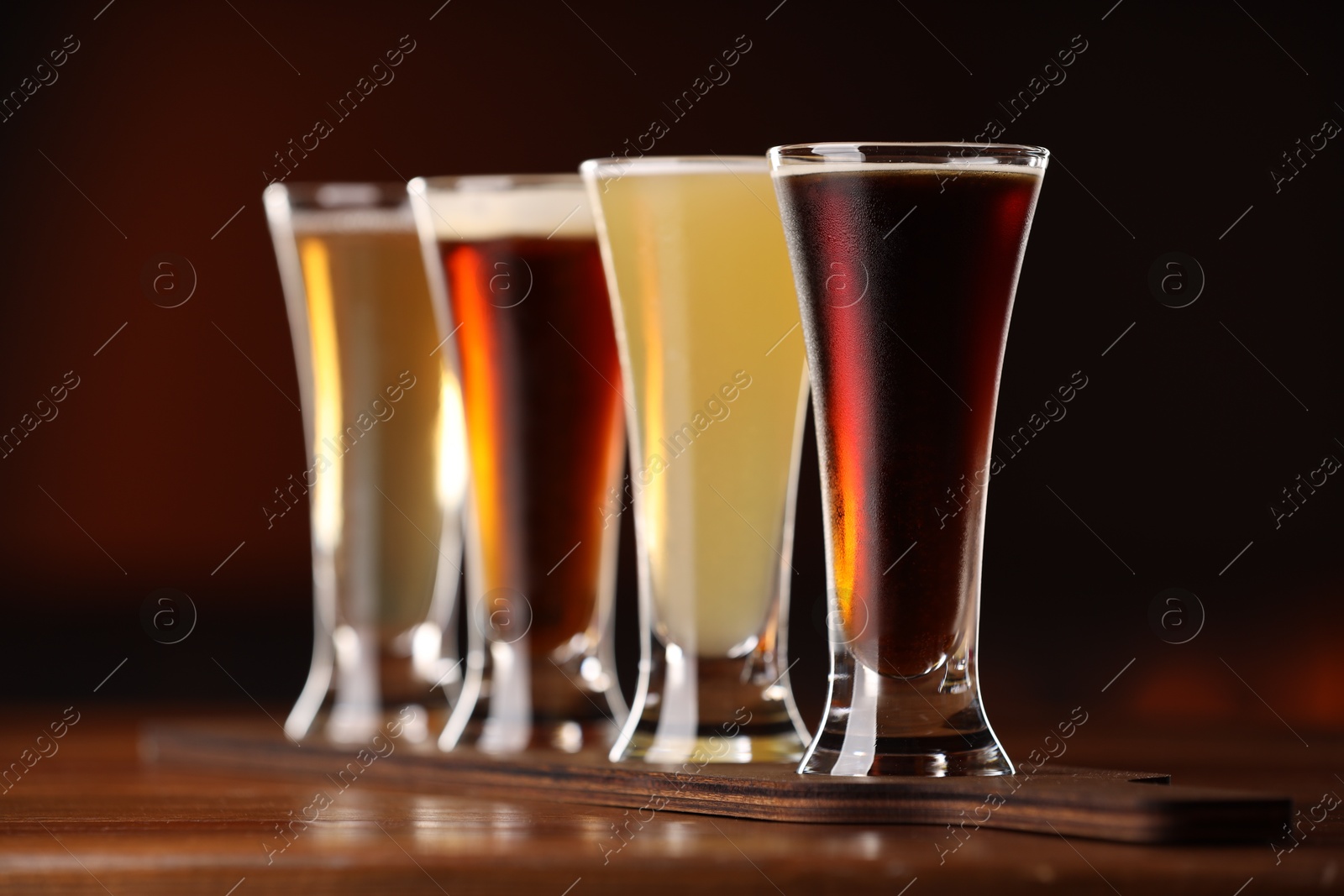 Photo of Glasses with different types of beer on wooden table against color background, closeup