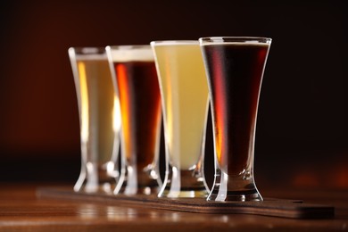 Photo of Glasses with different types of beer on wooden table against color background, closeup