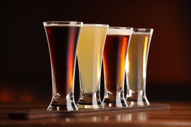 Photo of Glasses with different types of beer on wooden table against color background, closeup