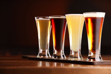 Photo of Glasses with different types of beer on wooden table against color background, closeup