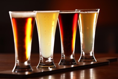 Glasses with different types of beer on wooden table against color background, closeup