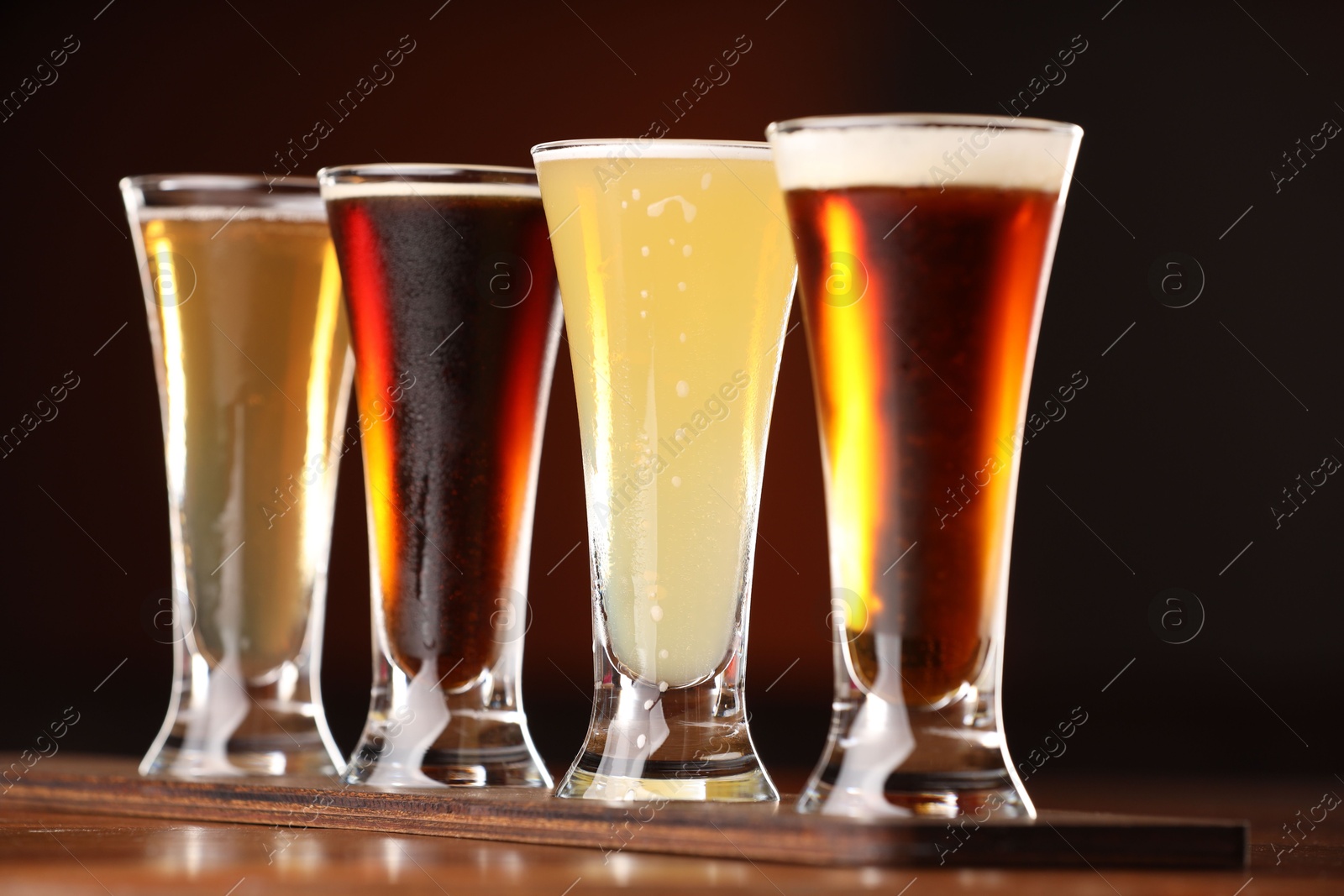 Photo of Glasses with different types of beer on wooden table against color background, closeup