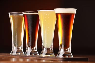 Photo of Glasses with different types of beer on wooden table against color background, closeup