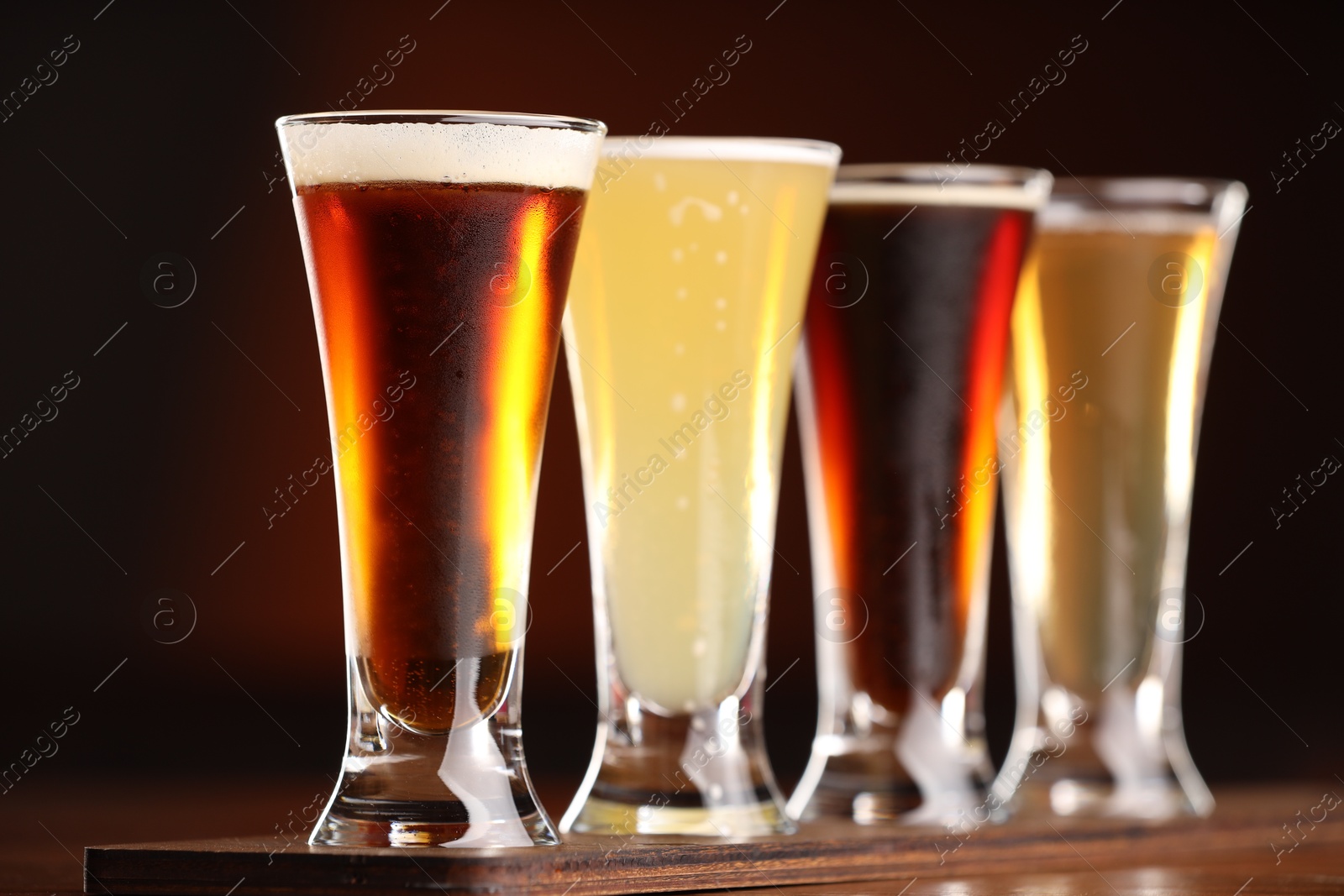 Photo of Glasses with different types of beer on wooden table against color background, closeup