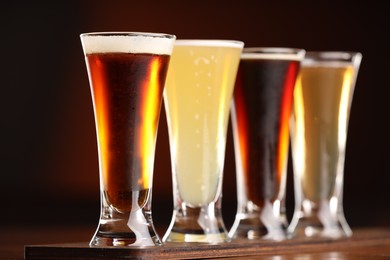 Photo of Glasses with different types of beer on wooden table against color background, closeup