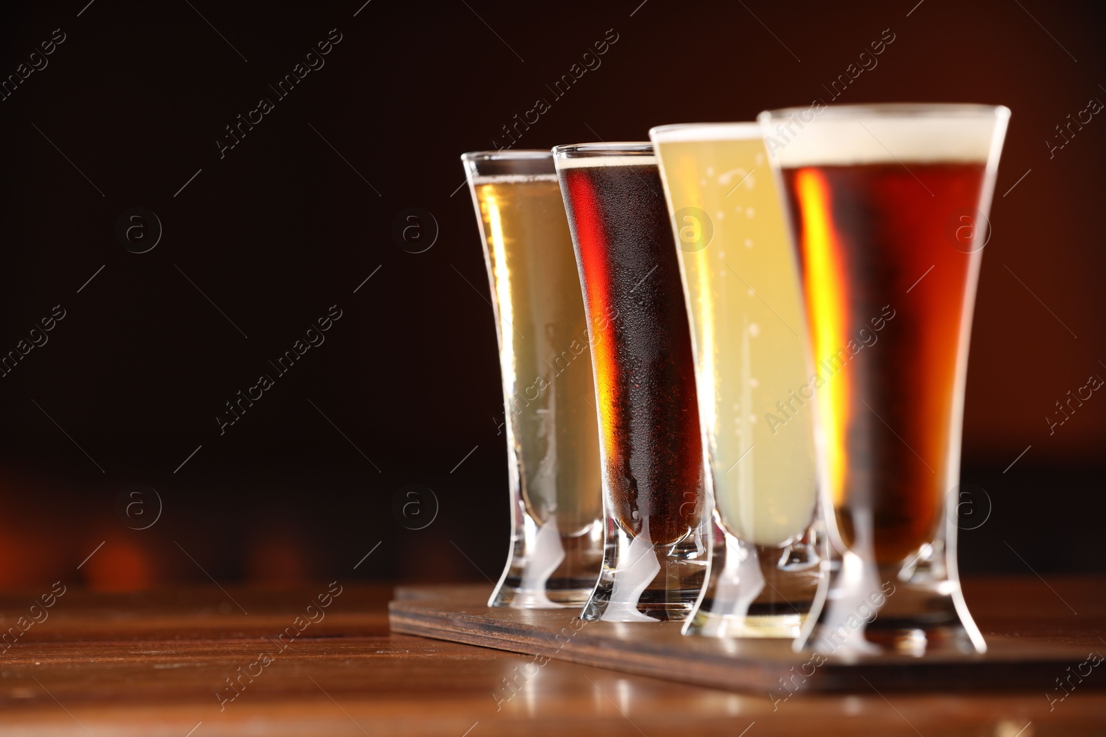 Photo of Glasses with different types of beer on wooden table against color background, closeup. Space for text