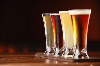 Photo of Glasses with different types of beer on wooden table against color background, closeup. Space for text