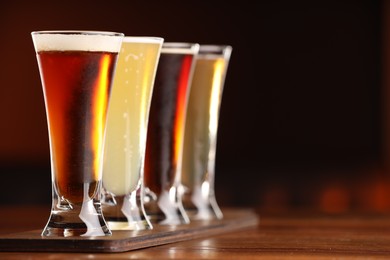 Photo of Glasses with different types of beer on wooden table against color background, closeup. Space for text