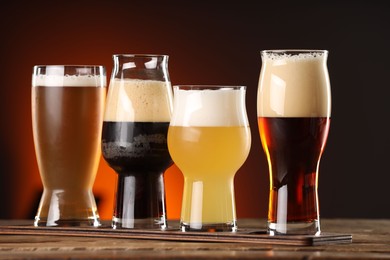 Photo of Glasses with different types of beer on wooden table against color background