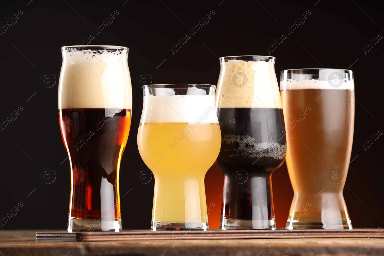 Photo of Glasses with different types of beer on wooden table against dark background