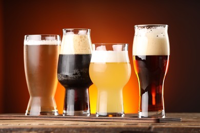 Photo of Glasses with different types of beer on wooden table against color background