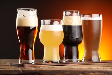 Photo of Glasses with different types of beer on wooden table against color background, closeup