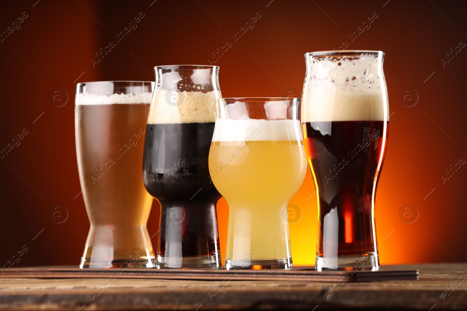 Photo of Glasses with different types of beer on wooden table against color background