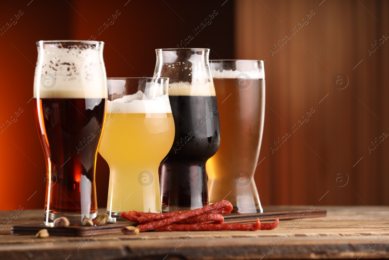 Photo of Glasses with different types of beer and snacks on wooden table indoors