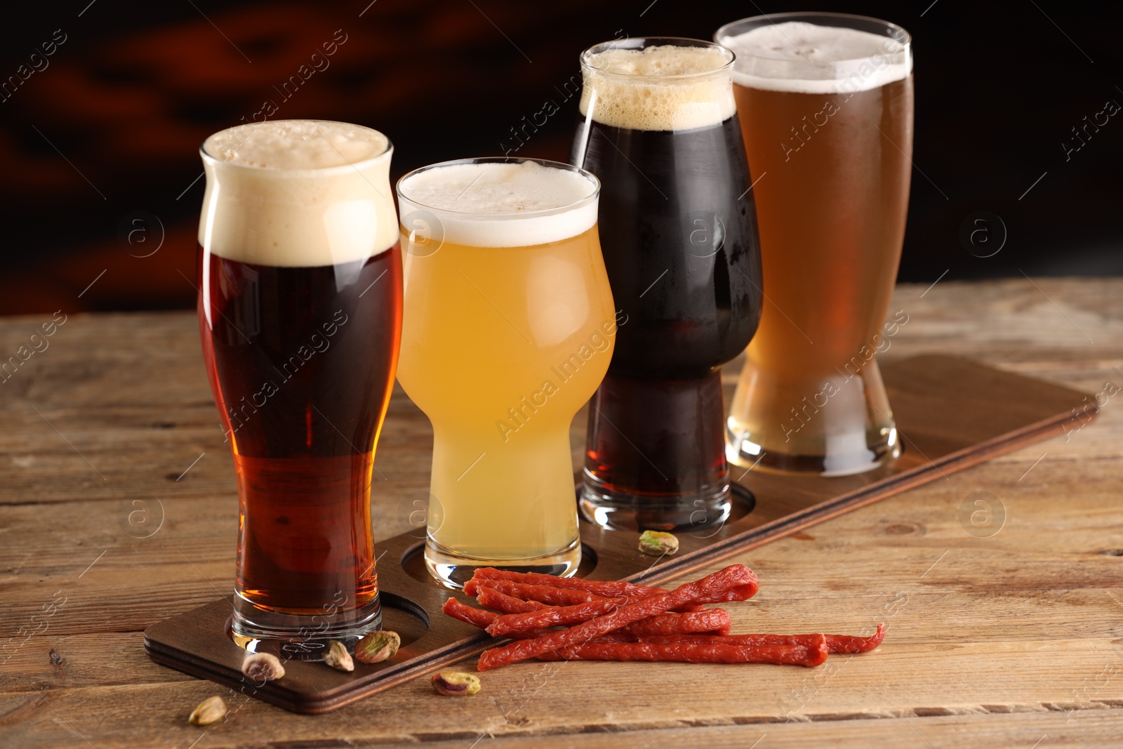 Photo of Glasses with different types of beer and snacks on wooden table indoors