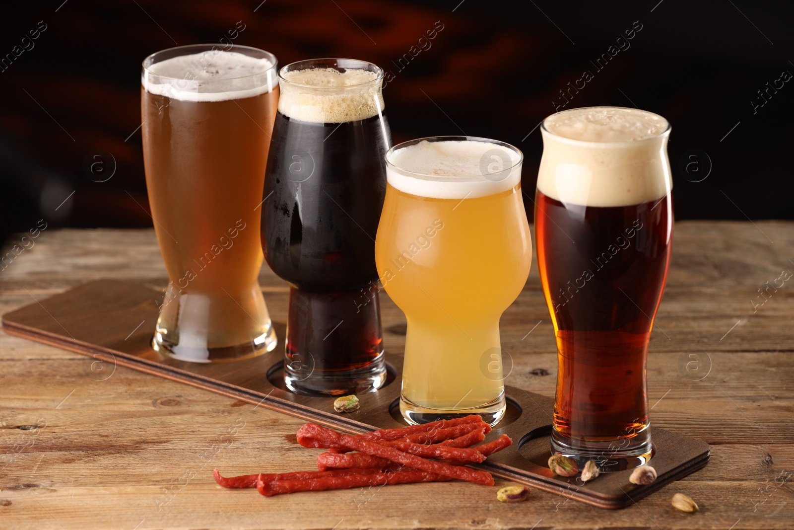 Photo of Glasses with different types of beer and snacks on wooden table indoors