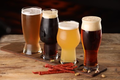 Photo of Glasses with different types of beer and snacks on wooden table indoors