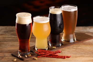 Photo of Glasses with different types of beer and snacks on wooden table indoors