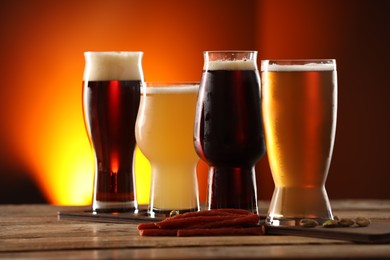 Photo of Glasses with different types of beer and snacks on wooden table against color background