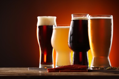 Photo of Glasses with different types of beer and snacks on wooden table against color background