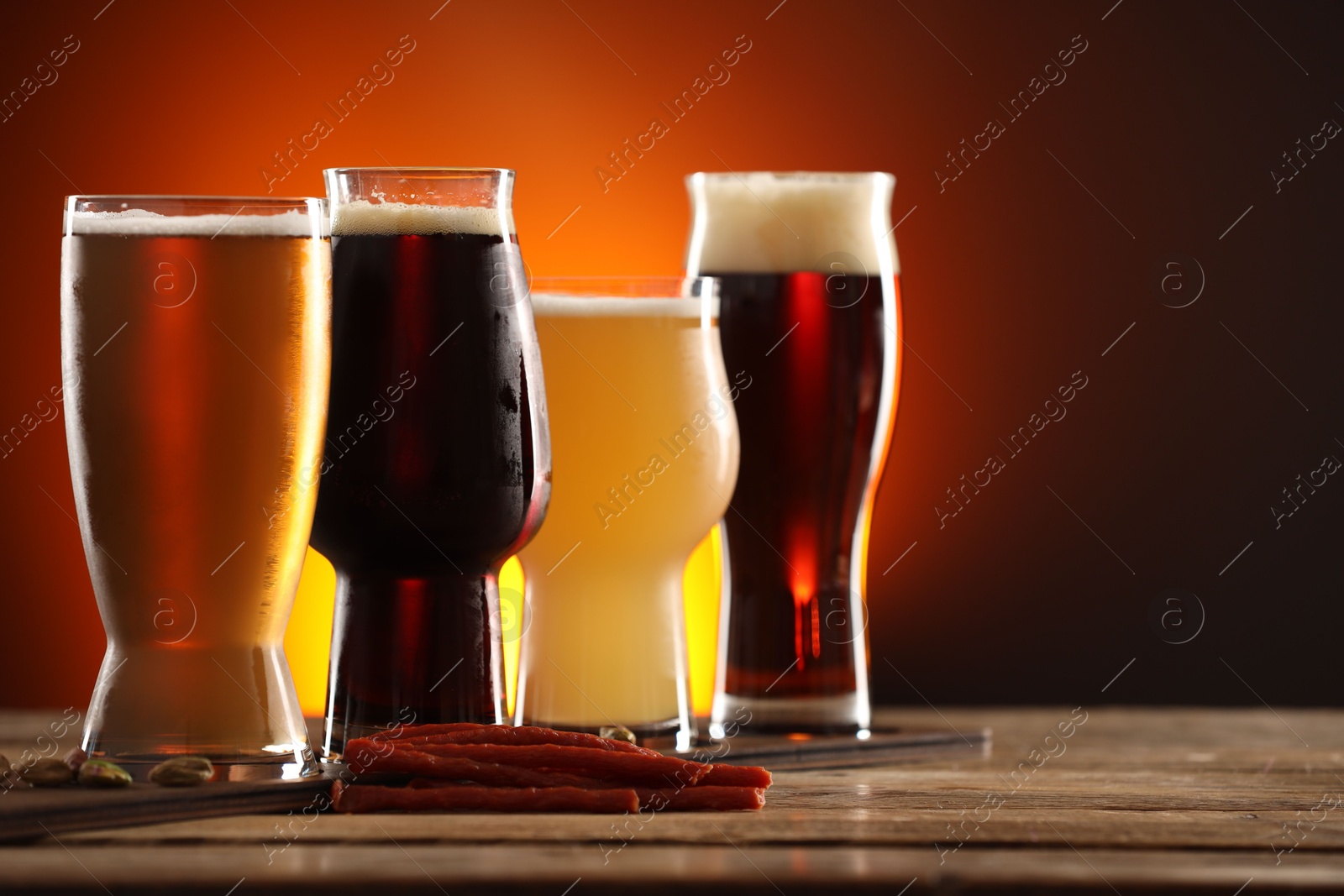 Photo of Glasses with different types of beer and snacks on wooden table against color background