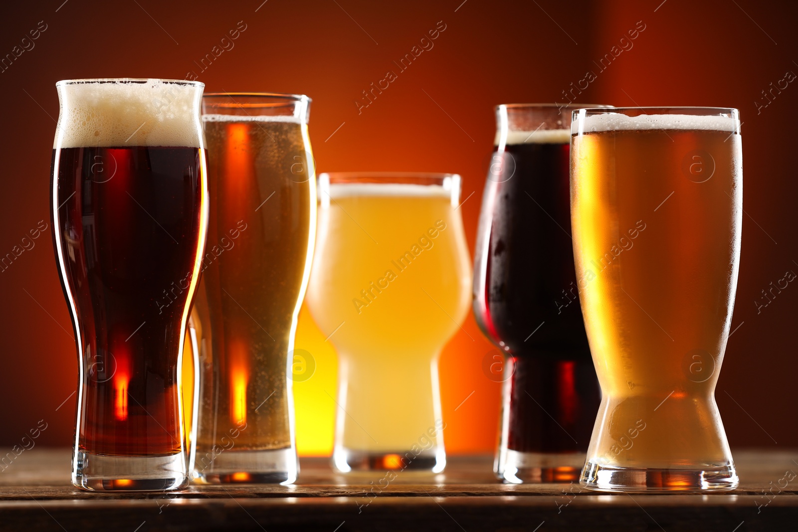 Photo of Glasses with different types of beer and snacks on wooden table against color background, closeup