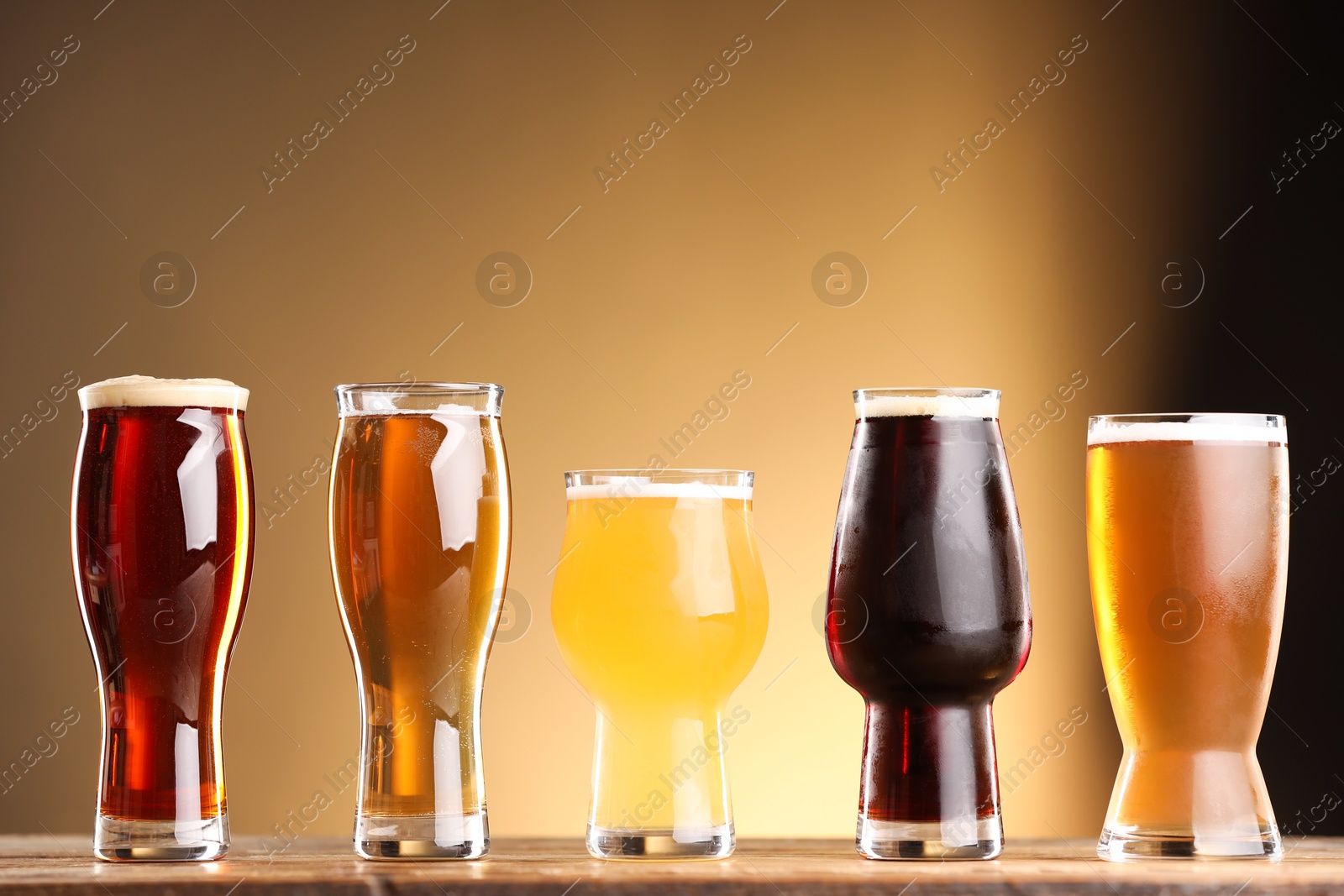 Photo of Glasses with different types of beer on wooden table against color background