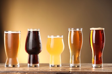 Photo of Glasses with different types of beer on wooden table against color background