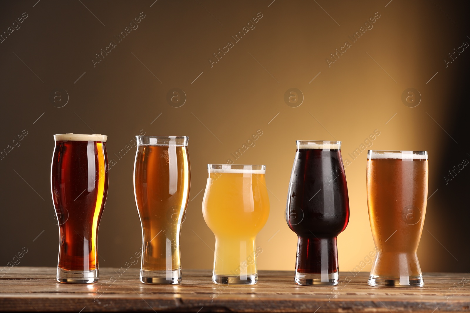 Photo of Glasses with different types of beer on wooden table against color background