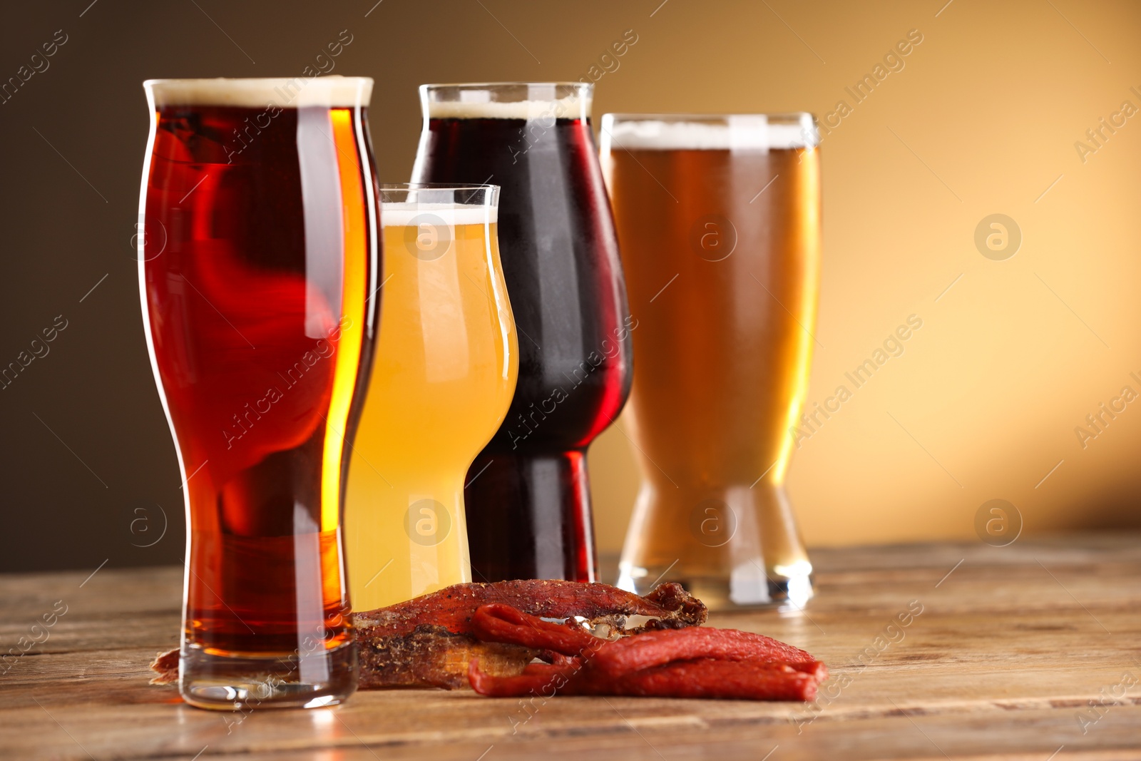 Photo of Glasses with different types of beer and snacks on wooden table against color background, closeup