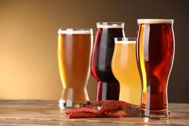 Photo of Glasses with different types of beer and snacks on wooden table against color background, closeup