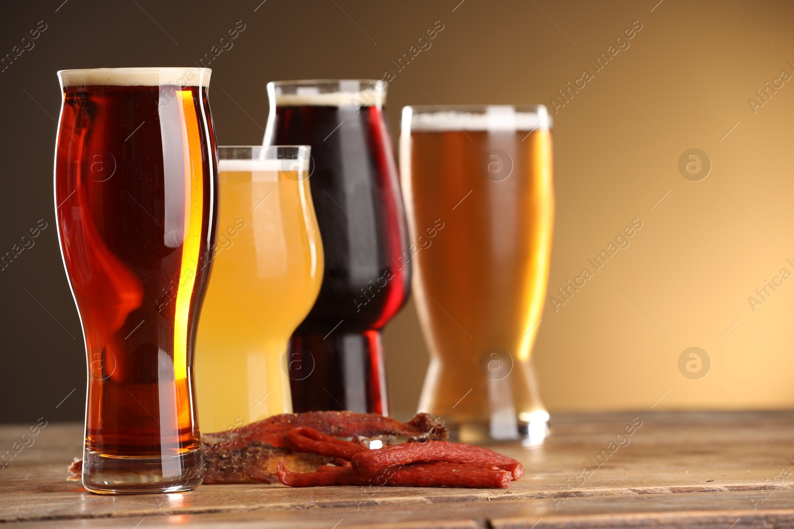 Photo of Glasses with different types of beer and snacks on wooden table against color background, closeup