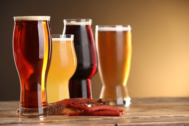 Photo of Glasses with different types of beer and snacks on wooden table against color background, closeup