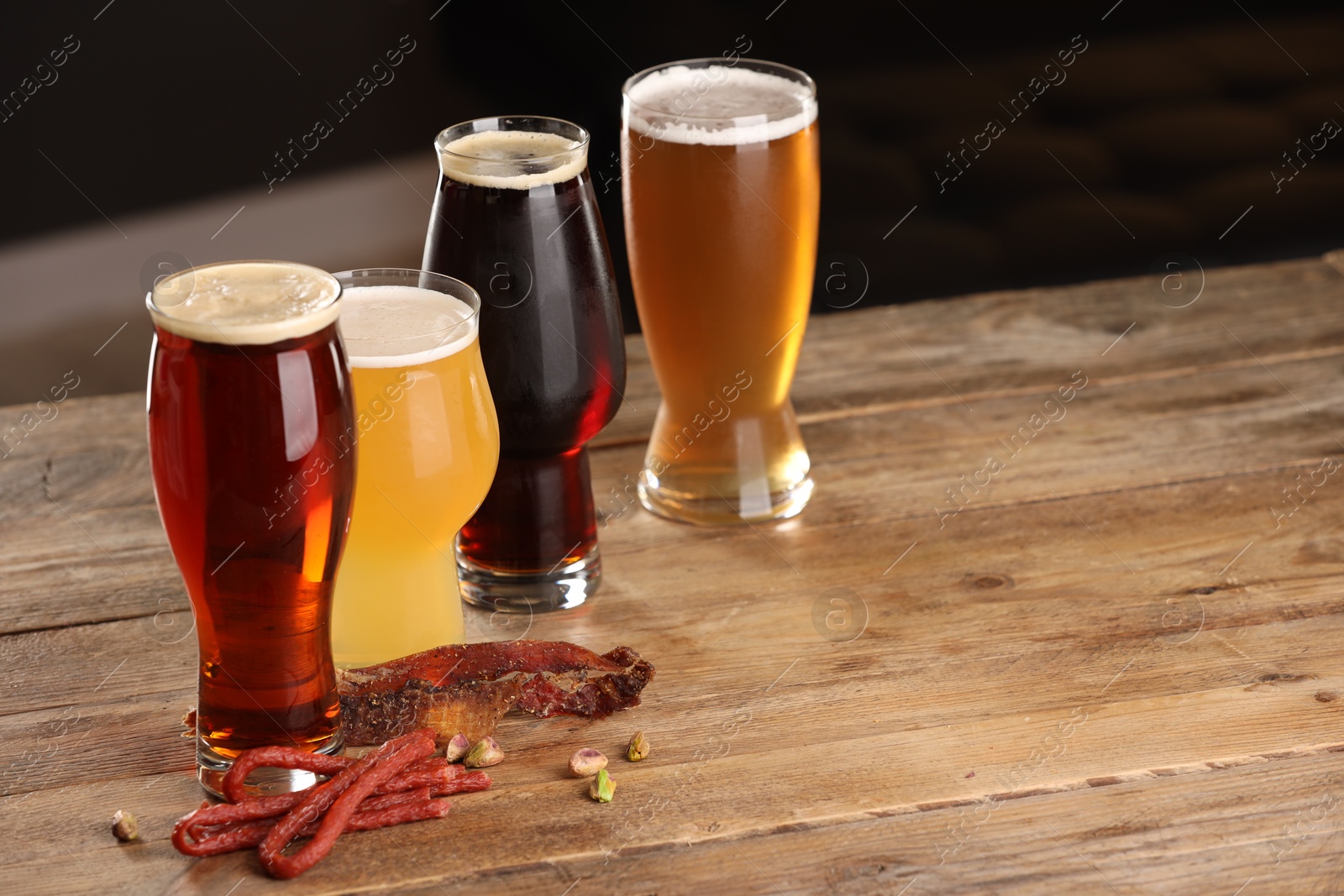 Photo of Glasses with different types of beer and snacks on wooden table. Space for text