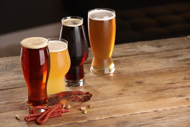 Photo of Glasses with different types of beer and snacks on wooden table. Space for text