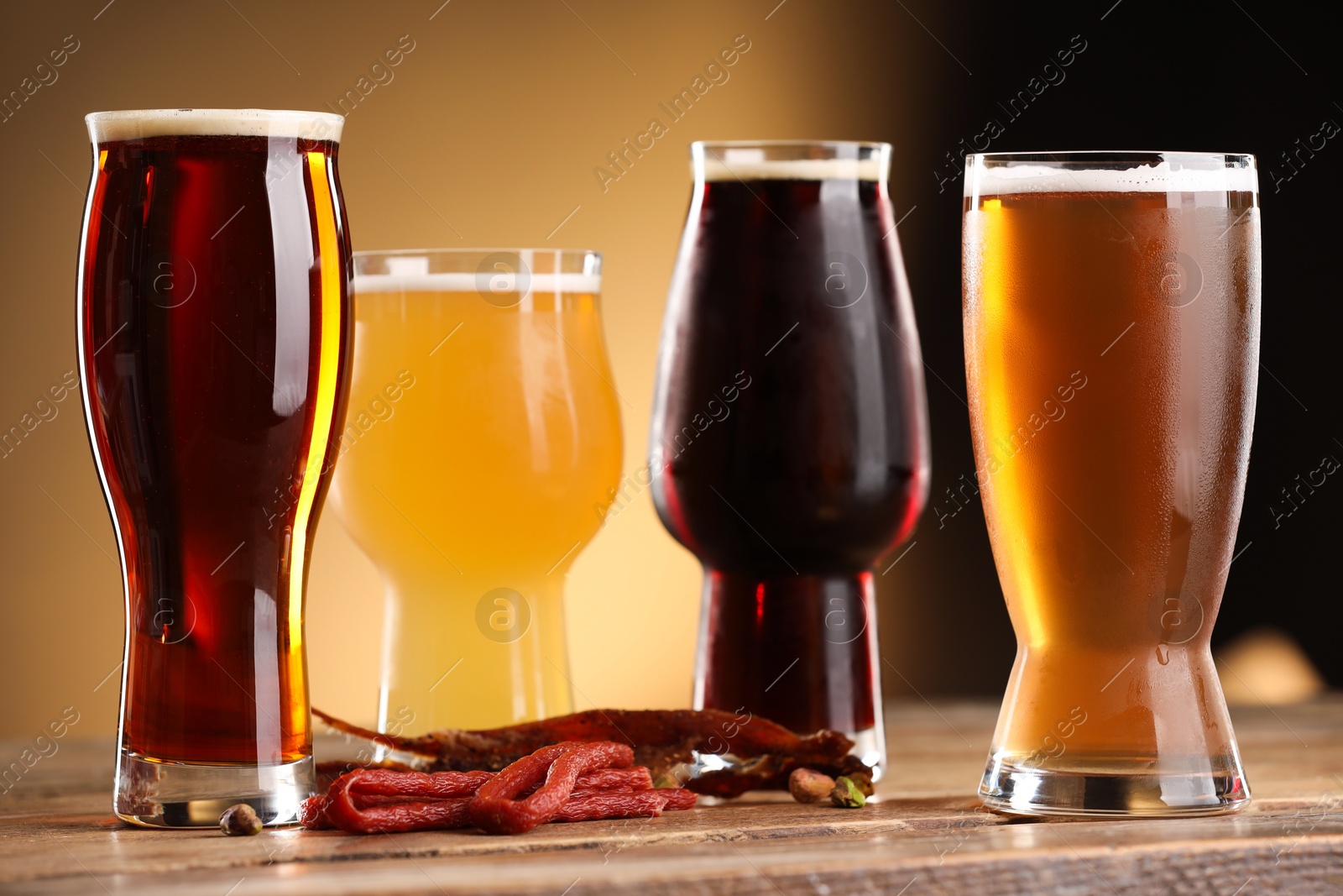 Photo of Glasses with different types of beer and snacks on wooden table against color background, closeup