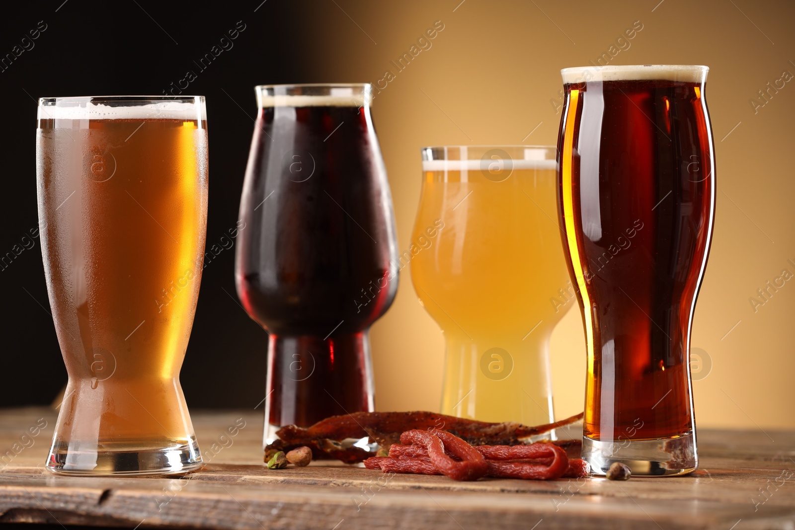 Photo of Glasses with different types of beer and snacks on wooden table against color background, closeup