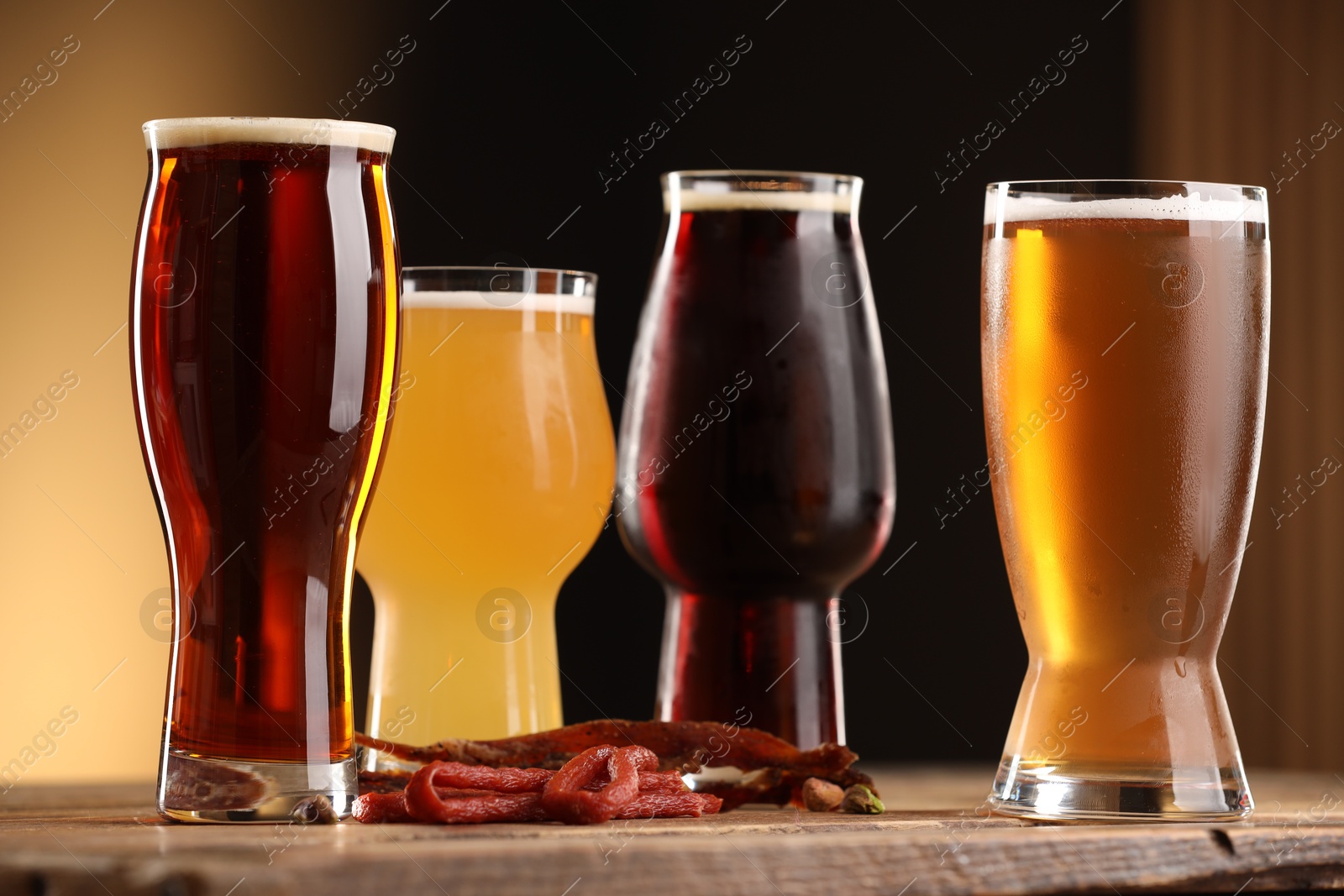 Photo of Glasses with different types of beer and snacks on wooden table against color background, closeup