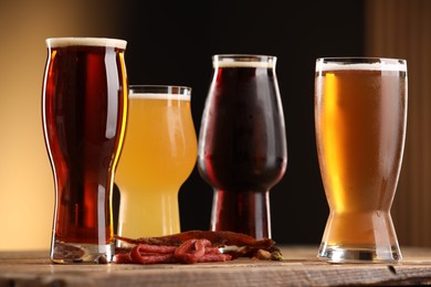 Photo of Glasses with different types of beer and snacks on wooden table against color background, closeup