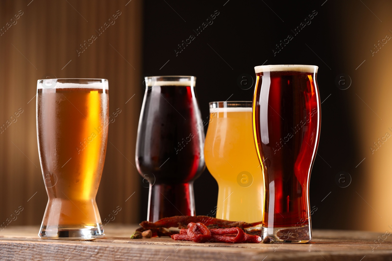 Photo of Glasses with different types of beer and snacks on wooden table against color background