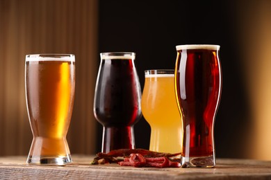 Photo of Glasses with different types of beer and snacks on wooden table against color background