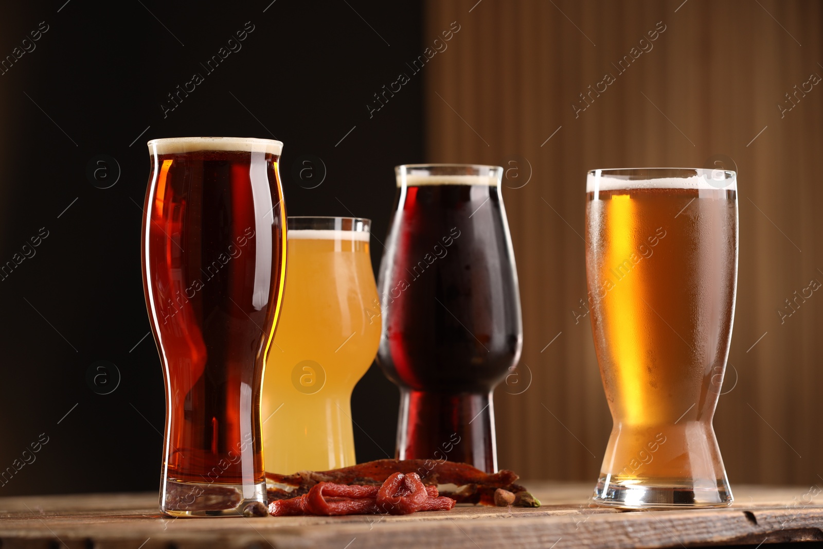 Photo of Glasses with different types of beer and snacks on wooden table against color background